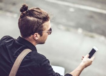 manbun styled man holding mobile