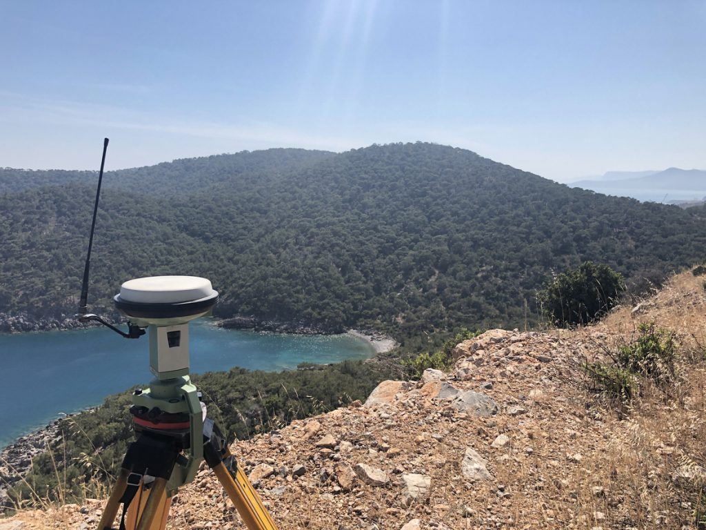 GNSS base receiver stands on the tripod at the hill top against sea at the background.